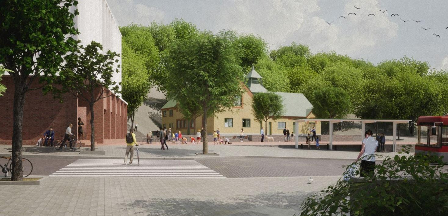 En urna med växtlighet i förgrunden, en väg och på andra sidan ser man ett litet torg framför en äldre byggnad och ett nytt hus skymtar på vänstersidan om lilla torget