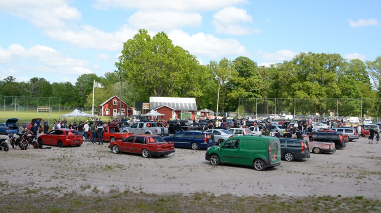 Många a-traktorer står i tre rader på en grusplan, människor rör sig mellan fordonen.