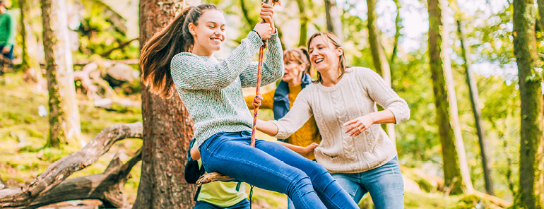 Familj som gungar i en skog, vid en slänt