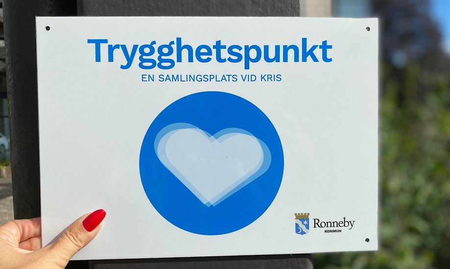 ljus skylt med text trygghetspunkt som hålls upp av en hand mot bakgrunden av en fastighet