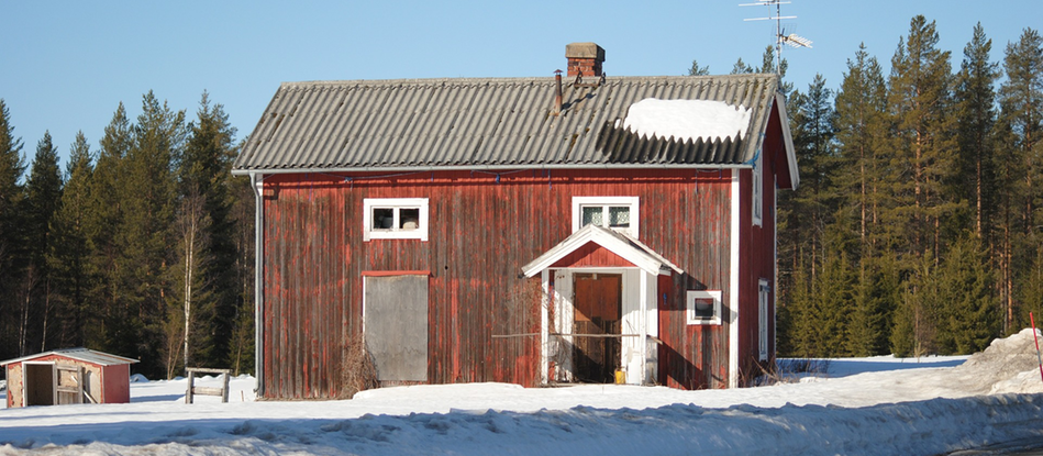 Ödehus i vinterskrud, rött tvåvåningshus i träpanel, farstukvist, vita knutar, brädor för fönstren, dåligt skick, barrskog i bakgrunden